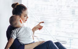 Унылая мать сидя с ее младенцем на windowsill, смотря вне окно и ждать что-то Младенец лежит на ` мамы стоковые изображения Унылая мать сидя с ее младенцем на windowsill, смотря вне окно и ждать что-то Младенец лежит на ` мамы стоковые изображения
