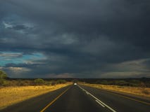 Управлять offroad автомобилем через черное идя дождь облако на поездке шоссе через ландшафт высушенной травы саванны стоковые фотографии rf Управлять offroad автомобилем через черное идя дождь облако на поездке шоссе через ландшафт высушенной травы саванны стоковые фотографии rf