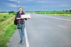 Усмехаясь автостопщик женщины на дороге держит пустую доску стоковые изображения Усмехаясь автостопщик женщины на дороге держит пустую доску стоковые изображения