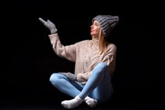 Усмехаясь белокурая девушка в серых связанных перчатках, шляпа и свитер сидя на черном поле с пересеченными ногами с ее глазами с стоковая фотография Усмехаясь белокурая девушка в серых связанных перчатках, шляпа и свитер сидя на черном поле с пересеченными ногами с ее глазами с стоковая фотография