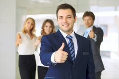 Усмехаясь бизнесмен в офисе с коллегами на заднем плане большие пальцы руки вверх стоковая фотография rf Усмехаясь бизнесмен в офисе с коллегами на заднем плане большие пальцы руки вверх стоковая фотография rf