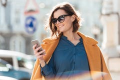 Усмехаясь вскользь женщина в солнечных очках смотря мобильный телефон стоковые фотографии rf Усмехаясь вскользь женщина в солнечных очках смотря мобильный телефон стоковые фотографии rf