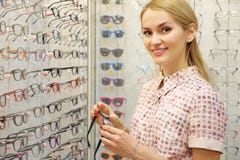 Усмехаясь молодая женщина пробуя новые стекла в магазине optician стоковое изображение rf Усмехаясь молодая женщина пробуя новые стекла в магазине optician стоковое изображение rf