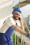 Усмехаясь рабочий-строитель в работе оборудует и шлем на голове говоря на телефоне Работа на большой возвышенности стоковые изображения rf Усмехаясь рабочий-строитель в работе оборудует и шлем на голове говоря на телефоне Работа на большой возвышенности стоковые изображения rf