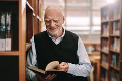 Усмехаясь старший человек смотря положение книги в библиотеке стоковое фото Усмехаясь старший человек смотря положение книги в библиотеке стоковое фото