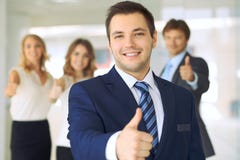 Успешные молодые бизнесмены показывая большие пальцы руки поднимают знак пока стоящ в офисе более interier стоковое фото Успешные молодые бизнесмены показывая большие пальцы руки поднимают знак пока стоящ в офисе более interier стоковое фото