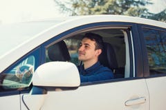 Успешный молодой человек управляя его новым белым автомобилем держит руку на руле смотря вперед счастливый чувствовать безопасен стоковые изображения rf Успешный молодой человек управляя его новым белым автомобилем держит руку на руле смотря вперед счастливый чувствовать безопасен стоковые изображения rf