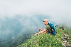 Уставший интернет просматривать человека backpacker используя смартфон наслаждаясь пасмурным дном долины идя туманной горой пасму стоковые фотографии rf Уставший интернет просматривать человека backpacker используя смартфон наслаждаясь пасмурным дном долины идя туманной горой пасму стоковые фотографии rf
