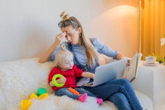 Утомленная мама пробуя работать на компьютере стоковое изображение Утомленная мама пробуя работать на компьютере стоковое изображение