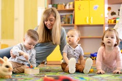 Учитель питомника смотря после детей в daycare Малыши маленьких ребят играют вместе с отработочными игрушками стоковые фотографии rf Учитель питомника смотря после детей в daycare Малыши маленьких ребят играют вместе с отработочными игрушками стоковые фотографии rf