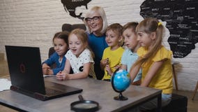 Учитель помогая кавказским детям на компьютерном терминале в начальной школе Усмехаясь дети школы используя компьютер с акции видеоматериалы Учитель помогая кавказским детям на компьютерном терминале в начальной школе Усмехаясь дети школы используя компьютер с акции видеоматериалы
