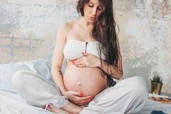 Фото урожая красивой беременной молодой женщины девушки с длинным вьющиеся волосы сидя в представлении лотоса на кровати Йога и п стоковое фото rf Фото урожая красивой беременной молодой женщины девушки с длинным вьющиеся волосы сидя в представлении лотоса на кровати Йога и п стоковое фото rf