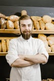 Харизматический хлебопек стоит на предпосылке полок со свежим хлебом стоковое фото rf Харизматический хлебопек стоит на предпосылке полок со свежим хлебом стоковое фото rf
