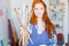Художник молодой женщины показывая пакостные paintbrushes в мастерской художника Стоковое Фото Художник молодой женщины показывая пакостные paintbrushes в мастерской художника Стоковое Фото