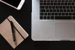Частично взгляд серебряной клавиатуры ноутбука со смартфоном и тетради с карандашем на темном деревянном столе стоковые изображения rf Частично взгляд серебряной клавиатуры ноутбука со смартфоном и тетради с карандашем на темном деревянном столе стоковые изображения rf