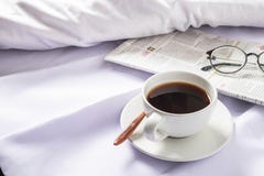 Чашка кофе и газета на белой кровати в утре стоковое фото Чашка кофе и газета на белой кровати в утре стоковое фото