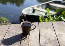 Чашка чаю с ложкой на деревянных предпосылке, реке и шлюпке позади стоковое фото Чашка чаю с ложкой на деревянных предпосылке, реке и шлюпке позади стоковое фото
