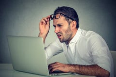 Человек при стекла имея проблемы зрения смущенные с програмным обеспечением компьтер-книжки стоковое изображение Человек при стекла имея проблемы зрения смущенные с програмным обеспечением компьтер-книжки стоковое изображение