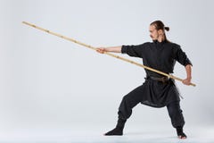 Человек ninja, в специальном черном кимоно, разрабатывает метод поражать с воюя бамбуковой ручкой стоковая фотография rf Человек ninja, в специальном черном кимоно, разрабатывает метод поражать с воюя бамбуковой ручкой стоковая фотография rf