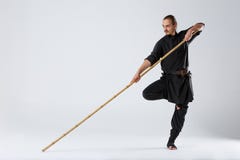 Человек ninja в черном кимоно, стоя в воюя позиции на одной ноге и держа воюя ручку стоковое фото rf Человек ninja в черном кимоно, стоя в воюя позиции на одной ноге и держа воюя ручку стоковое фото rf