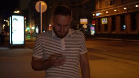 Человек в пребывании striped рубашки на улице и взгляде в телефоне Очень удивленный Бородатый красивый парень с телефоном в руке видеоматериал Человек в пребывании striped рубашки на улице и взгляде в телефоне Очень удивленный Бородатый красивый парень с телефоном в руке видеоматериал