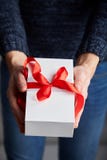 Человек держа белую подарочную коробку с красной лентой в его руках стоковое изображение Человек держа белую подарочную коробку с красной лентой в его руках стоковое изображение