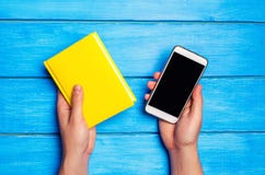 Человек держит Желтую книгу и телефон на голубой деревянной предпосылке Выбор между исследованием и телефоном Наркомания телефона стоковые изображения rf Человек держит Желтую книгу и телефон на голубой деревянной предпосылке Выбор между исследованием и телефоном Наркомания телефона стоковые изображения rf