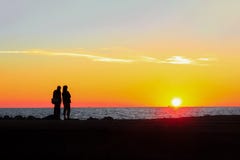 Человек и женщина восхищают красочный заход солнца на пляже стоковые фотографии rf Человек и женщина восхищают красочный заход солнца на пляже стоковые фотографии rf