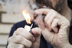 Человек предусматриванный в сигаре освещения дыма с лихтером металла стоковая фотография rf Человек предусматриванный в сигаре освещения дыма с лихтером металла стоковая фотография rf