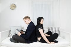 Человек работая на планшете и сидя на кровати спина к спине к ее девушке стоковое фото rf Человек работая на планшете и сидя на кровати спина к спине к ее девушке стоковое фото rf