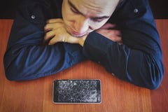 Человек смотрит его сломленный телефон лежа на деревянном столе с унылым взглядом стоковые фото Человек смотрит его сломленный телефон лежа на деревянном столе с унылым взглядом стоковые фото