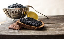 Черная икра в серебряном шаре с хлебом и лимоном на деревянной предпосылке стоковое изображение rf Черная икра в серебряном шаре с хлебом и лимоном на деревянной предпосылке стоковое изображение rf