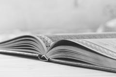 Черно-белое фото открытой книги на таблице, селективные фокус и отмелый стоковое изображение Черно-белое фото открытой книги на таблице, селективные фокус и отмелый стоковое изображение