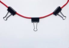 Черный бумажный зажим связывателя вися на изоляте красной веревочки на белой предпосылке стоковая фотография Черный бумажный зажим связывателя вися на изоляте красной веревочки на белой предпосылке стоковая фотография
