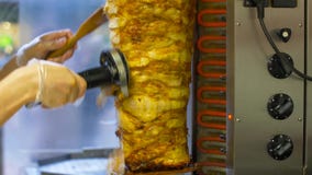Шеф-повар отрезая мясо doner от вертела на магазине kebab Шеф-повар отрезая мясо doner от вертела на магазине kebab