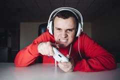Эмоциональный gamer играет игры дома на кнюппеле Молодой человек играет компютерные игры используя gamepad стоковое изображение rf Эмоциональный gamer играет игры дома на кнюппеле Молодой человек играет компютерные игры используя gamepad стоковое изображение rf