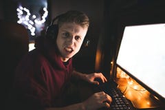 Эмоциональный gamer в наушниках, видеоиграх игр на домашнем компьютере, смотрит в камеру со злым взглядом стоковая фотография Эмоциональный gamer в наушниках, видеоиграх игр на домашнем компьютере, смотрит в камеру со злым взглядом стоковая фотография