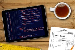 Эскиз wireframe вебсайта и программируя код на цифровой таблетке стоковая фотография Эскиз wireframe вебсайта и программируя код на цифровой таблетке стоковая фотография