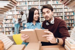 Этническая азиатская девушка и белый парень окруженные книгами в библиотеке Студенты книга чтения стоковые фотографии rf Этническая азиатская девушка и белый парень окруженные книгами в библиотеке Студенты книга чтения стоковые фотографии rf