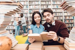 Этническая азиатская девушка и белый парень окруженные книгами в библиотеке Студенты книга чтения стоковые фото Этническая азиатская девушка и белый парень окруженные книгами в библиотеке Студенты книга чтения стоковые фото