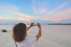 与浪漫天空智能手机的妇女照相在日落在沙滩,背面图,旅行的真人的环球 免版税库存照片 与浪漫天空智能手机的妇女照相在日落在沙滩,背面图,旅行的真人的环球 免版税库存照片