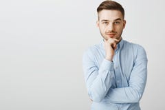 在时髦蓝领衬衣的聪明的雄心勃勃的英俊的男性握在下巴的手傻笑从兴趣和欢欣注视的 免版税库存照片 在时髦蓝领衬衣的聪明的雄心勃勃的英俊的男性握在下巴的手傻笑从兴趣和欢欣注视的 免版税库存照片