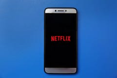 在智能手机屏幕上的Netflix商标在蓝色背景 供以人员拿着有Netflix商标的智能手机在屏幕上 库存图片 在智能手机屏幕上的Netflix商标在蓝色背景 供以人员拿着有Netflix商标的智能手机在屏幕上 库存图片
