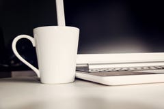 在桌上的白色杯子和膝上型计算机笔记本计算机 免版税库存照片 在桌上的白色杯子和膝上型计算机笔记本计算机 免版税库存照片