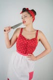 在红色圆点画报礼服和围裙的美好的少女身分,拿着一把大刀子和采摘她的牙,因为食物我 免版税库存图片 在红色圆点画报礼服和围裙的美好的少女身分,拿着一把大刀子和采摘她的牙,因为食物我 免版税库存图片