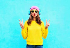 塑造相当耳机的凉快的女孩听到音乐的穿五颜六色的桃红色帽子黄色太阳镜和毛线衣在蓝色 免版税库存图片 塑造相当耳机的凉快的女孩听到音乐的穿五颜六色的桃红色帽子黄色太阳镜和毛线衣在蓝色 免版税库存图片