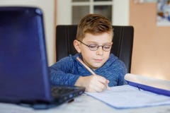 戴在家做学校家庭作业与笔记本的眼镜的愉快的健康孩子男孩 感兴趣的儿童文字杂文与 图库摄影 戴在家做学校家庭作业与笔记本的眼镜的愉快的健康孩子男孩 感兴趣的儿童文字杂文与 图库摄影