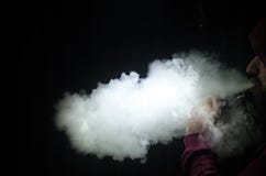 拿着mod的Vaping人 蒸气云彩 黑色背景 Vaping与很多烟的一根电子香烟 免版税库存图片 拿着mod的Vaping人 蒸气云彩 黑色背景 Vaping与很多烟的一根电子香烟 免版税库存图片