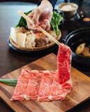拿着与使高有大理石花纹的纹理的手优质罕见的切片Wagyu A5牛肉与在方形的木板材的筷子 免版税图库摄影 拿着与使高有大理石花纹的纹理的手优质罕见的切片Wagyu A5牛肉与在方形的木板材的筷子 免版税图库摄影