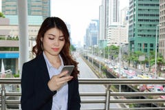 确信的年轻亚裔女商人在她的手上的注视着流动巧妙的电话都市大厦城市背景 图库摄影 确信的年轻亚裔女商人在她的手上的注视着流动巧妙的电话都市大厦城市背景 图库摄影